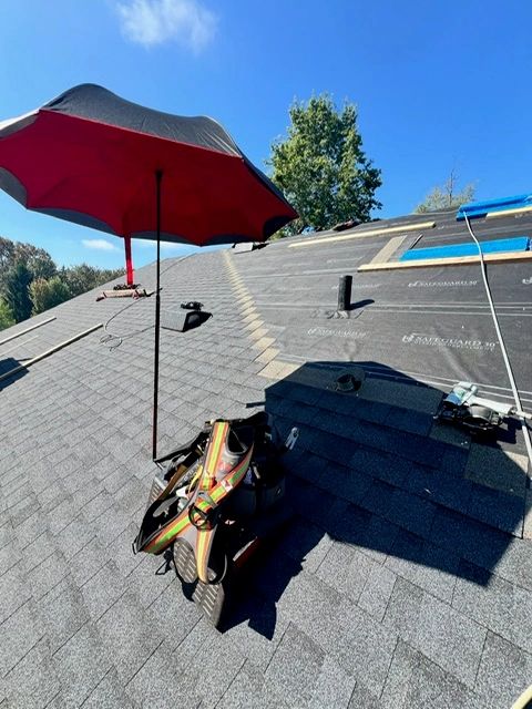 SunSafe Shield red umbrella shade mounted on a Pitch Hopper roofing wedge on an asphalt shingle roof